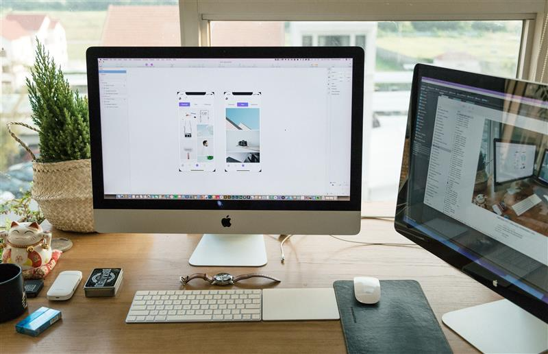 Designer workspace with an iMac showing mobile app screens in a design tool — iterative product improvement in progress